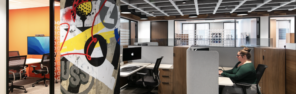 Modern office space with employees working at desks and a colorful graffiti-style pillar.